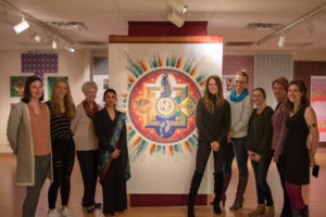 Graduate students stand beside brightly colored designs