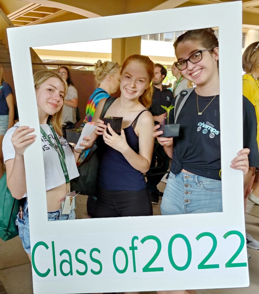 Students pose with plants in the Class of 2020 photo booth polaroid board.