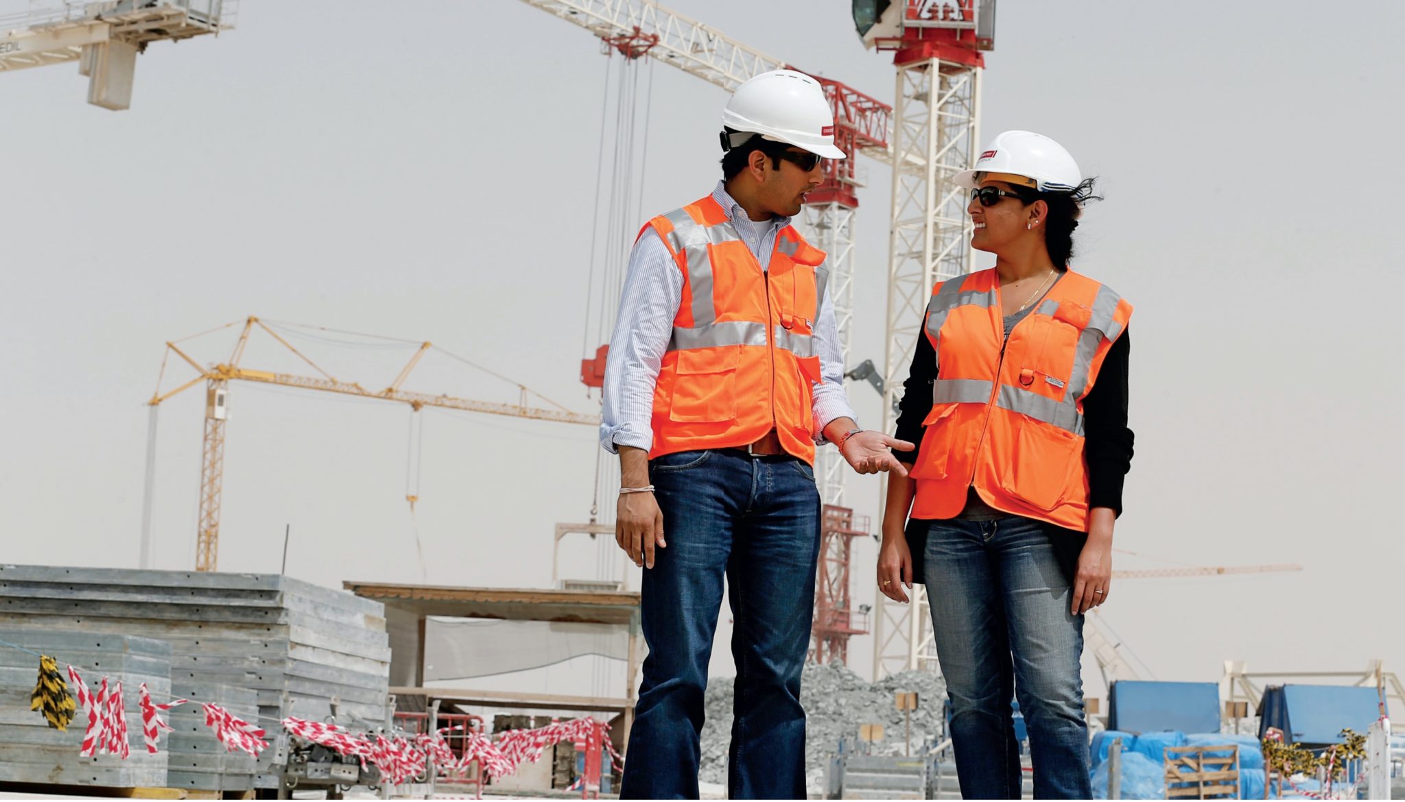 Sandeep and wife, Sirisha, stand in construction vests and hard hats with equipment in the background.
