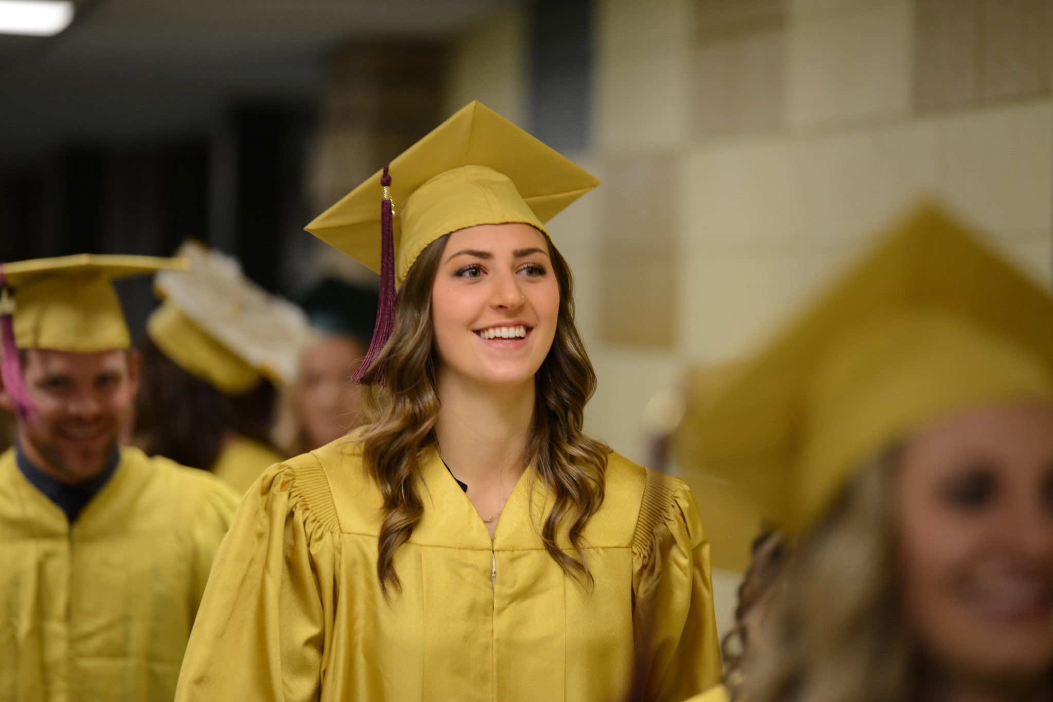 A female student smiling in a gold cap and gown.