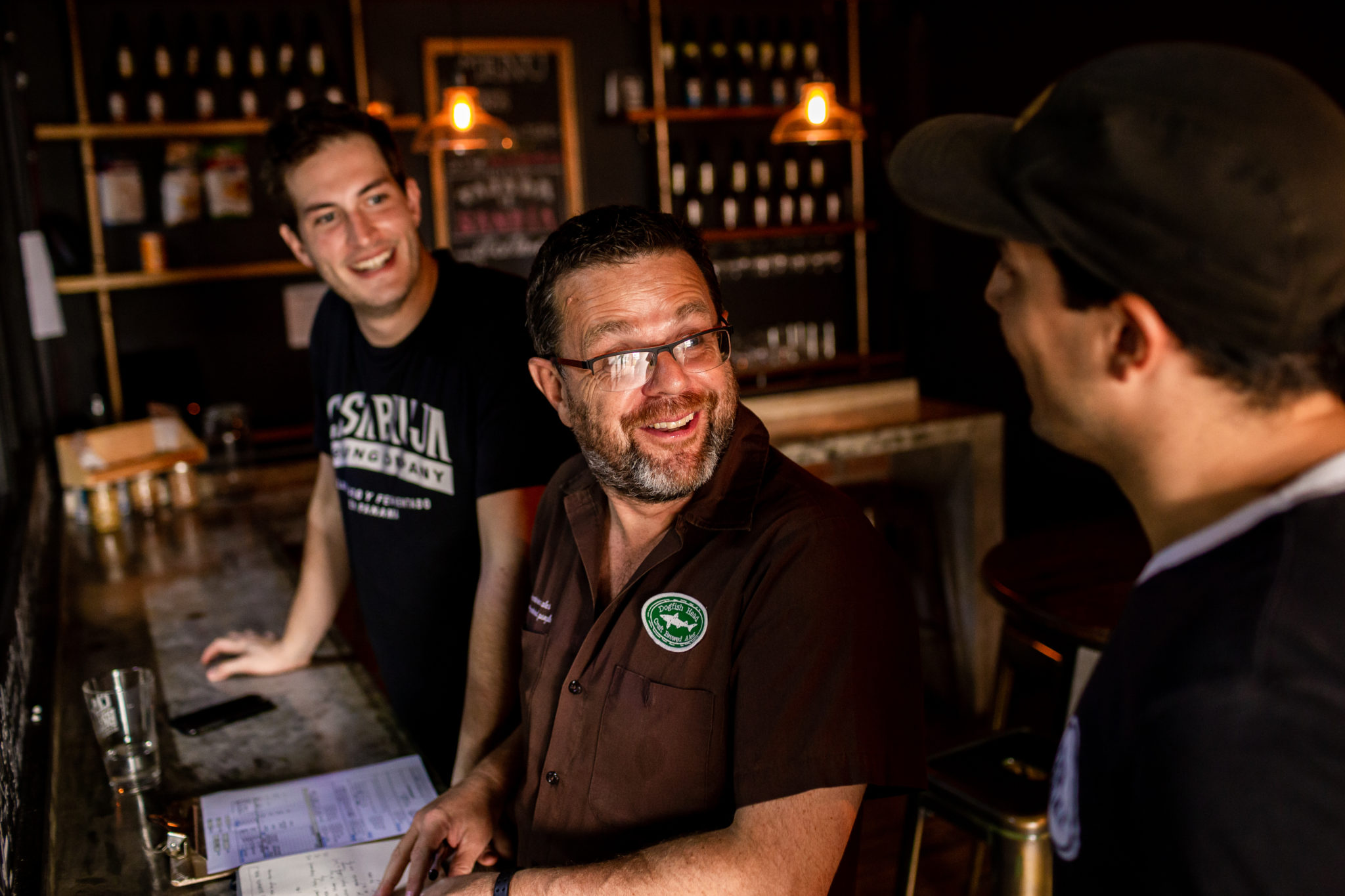 Three men laughing and chatting in the bar area of a brewery.