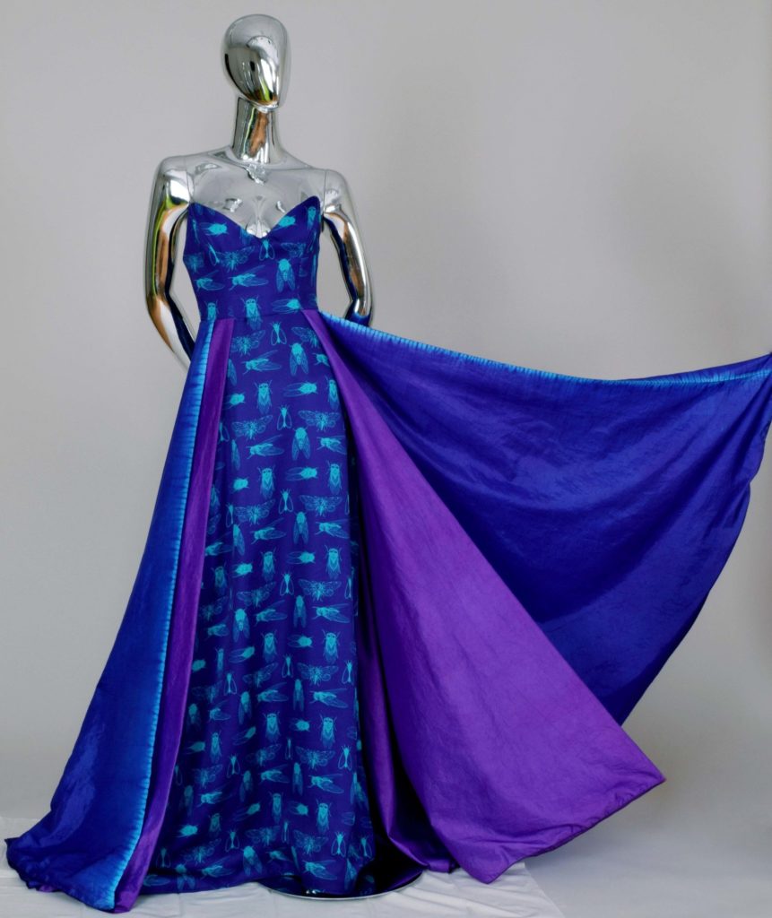 This royal blue ball gown features voluminous purple and blue skirts with a cicada print in light cerulean blue decorating the bodice and interior skirt panel.