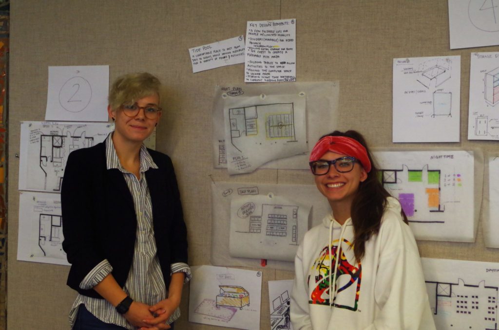 Students stand in front of a wall of designs.