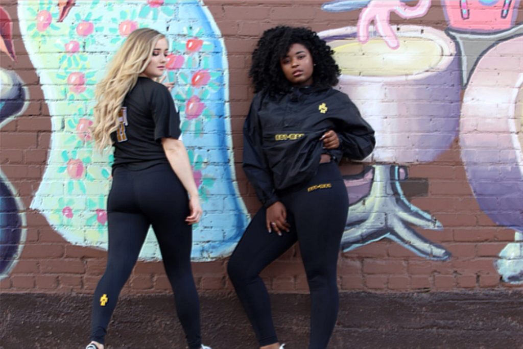 Two female models stand in front of a mural while wearing BotMan leggings and jackets.