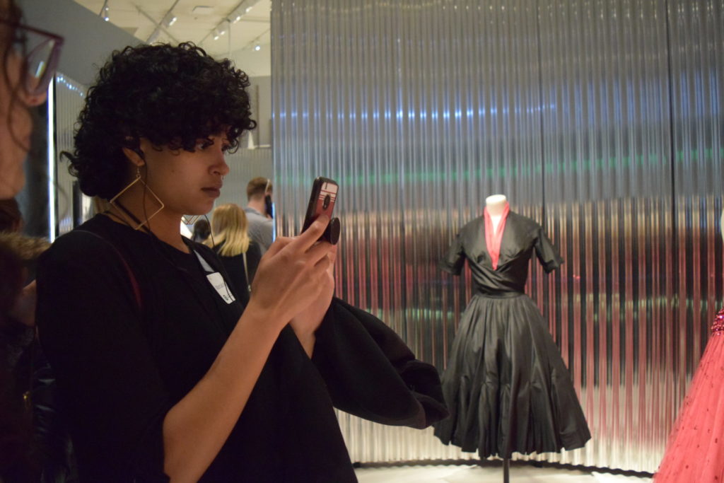 A student uses their cell phone to photograph a garment on display.