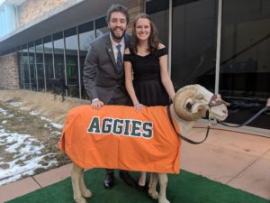 Caley and Taylor wearing formal attire in front of the stadium. Cam is wearing an orange Aggies blanket.