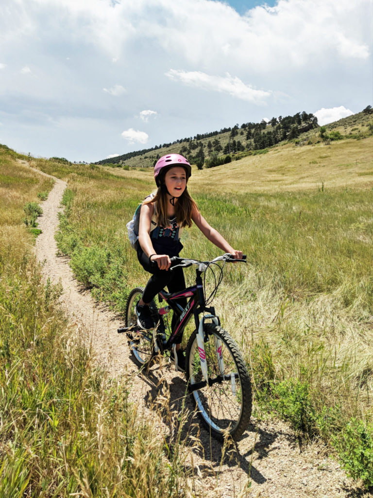 A girl mountain bikes down a grassy hill.