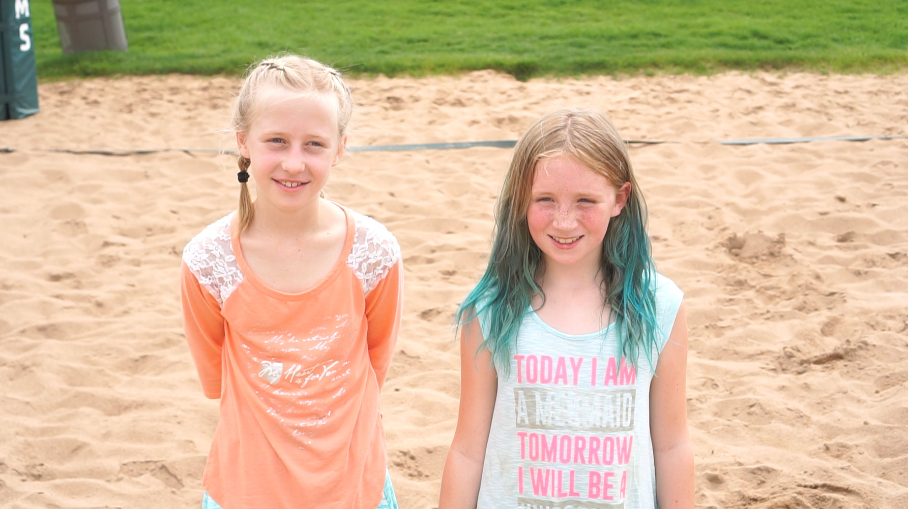 Two girls smile on a sand volleyball field.