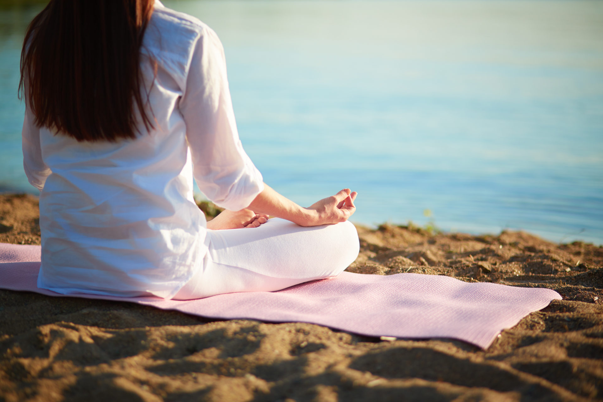 A woman sits on a beach while meditating.