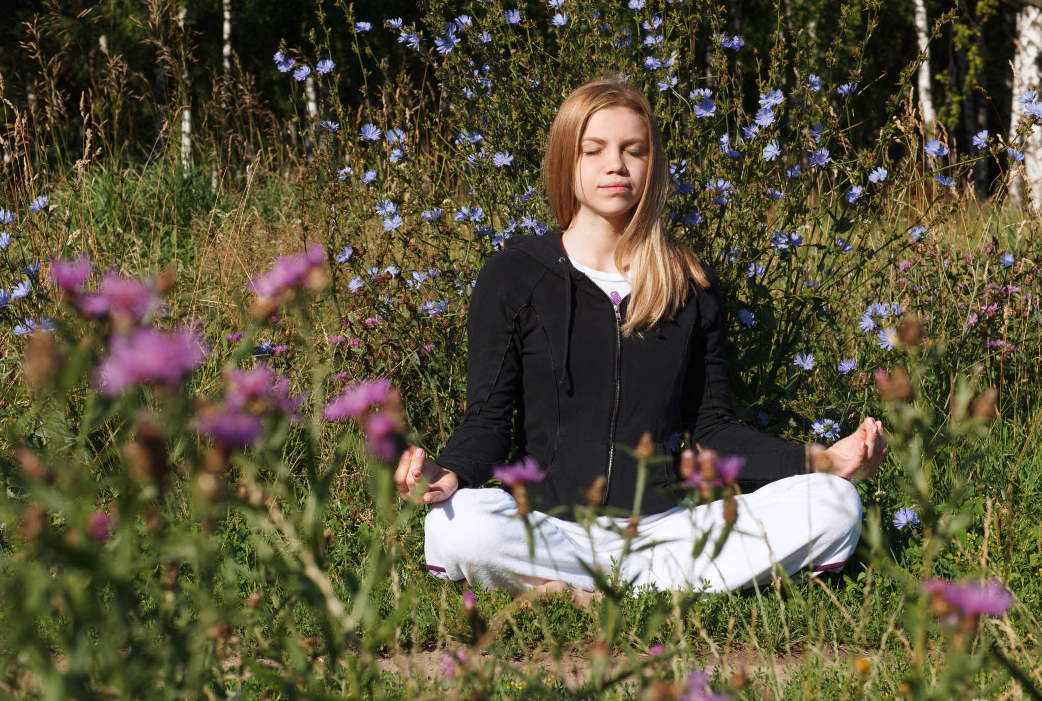 Woman meditating in a field of grass and flowers