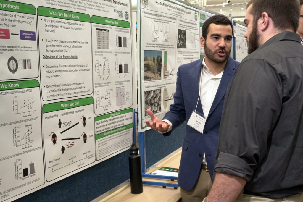 Raj Trikha presenting his research poster to a man reading about his research