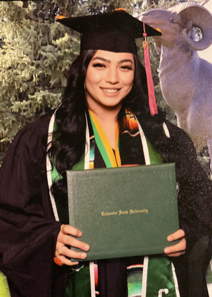 Jennifer Gomez stands in her commencement regalia holding her degree.