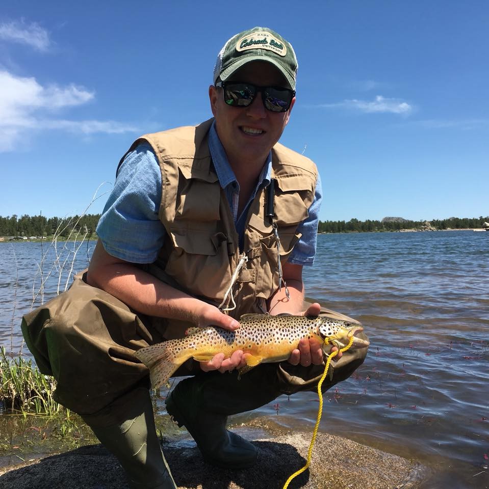 Alex Hendricks holding a fish near a lake.