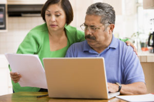 A couple together in the kitchen with a laptop and paperwork look concerned