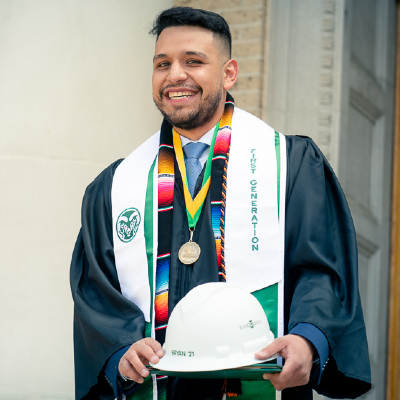 Bryan Flores Amezquita in graduation regalia holding his hardhat