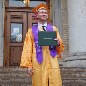 Peyton Woolverton on the admin building steps in his cap and gown