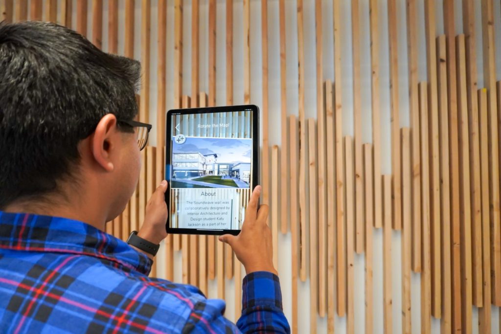 A student holds an ipad up to view the wall design and the app shares more information about how it was built