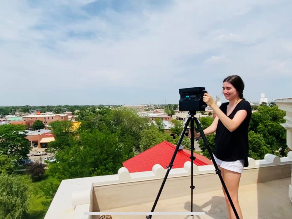 a young woman stands on a rooftop operating a 3D camera