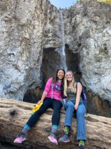 Kathrynn Hamada with a friend in front of a small cliff and waterfall