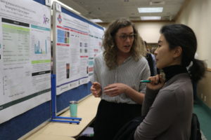 One person explaining their research poster to another person.