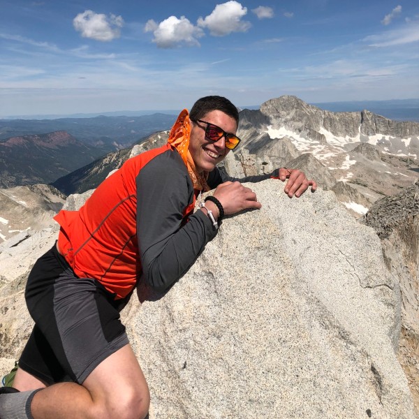 Travis Amato holding onto a rock edge on the top of a mountain