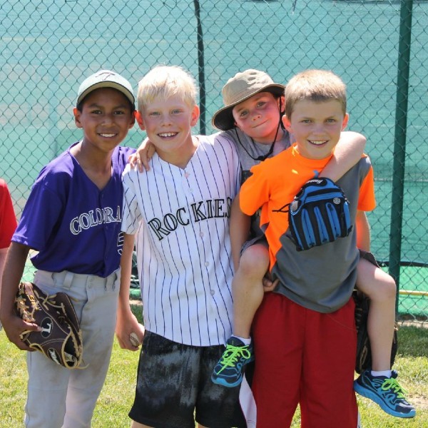Four children smile together on a baseball field