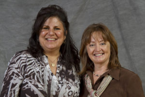 Two women smiling in front of a gray background
