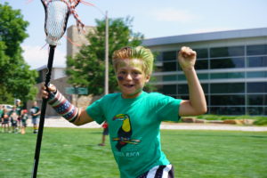 Boy celebrating with a lacrosse stick in his hand outdoors on a field