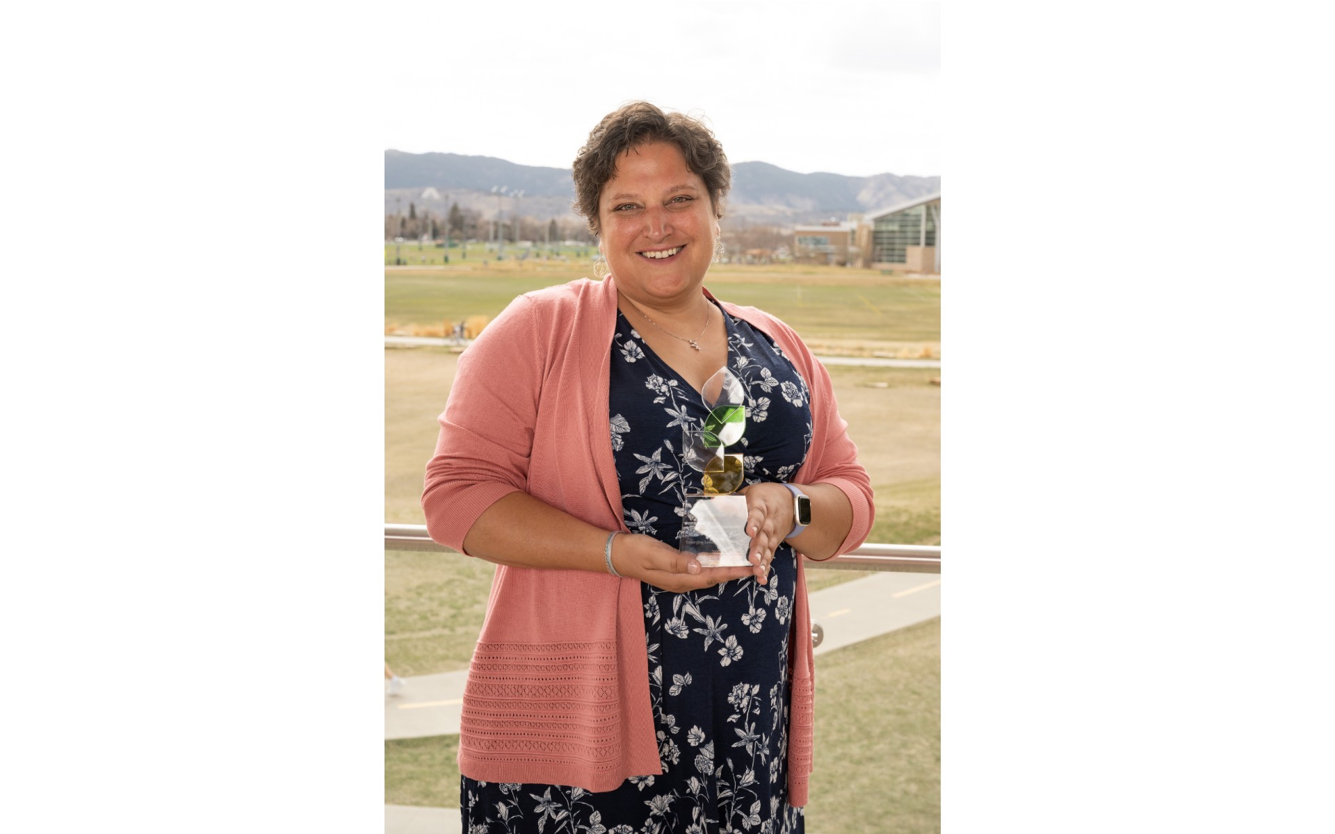 A woman holds an award with the CSU campus and foothills behind her