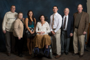 Large group photo of a family with college students. The woman in the center sits in a wheelchair.