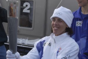 A woman in Olympic hat and jacket holds the torch