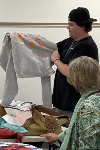 A person holds up a sweatshirt with orange spots for the class.
