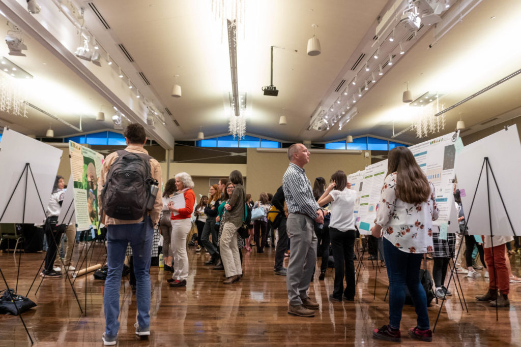 A wide shot of several people gathered around posters in the LSC ballroom