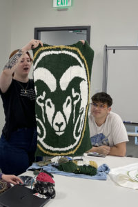 A woman holds up a quilt with the CSU logo on it