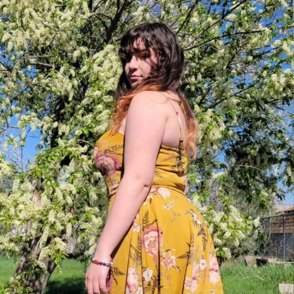 Sarah Fizer stands in a yellow dress near a blossom tree.