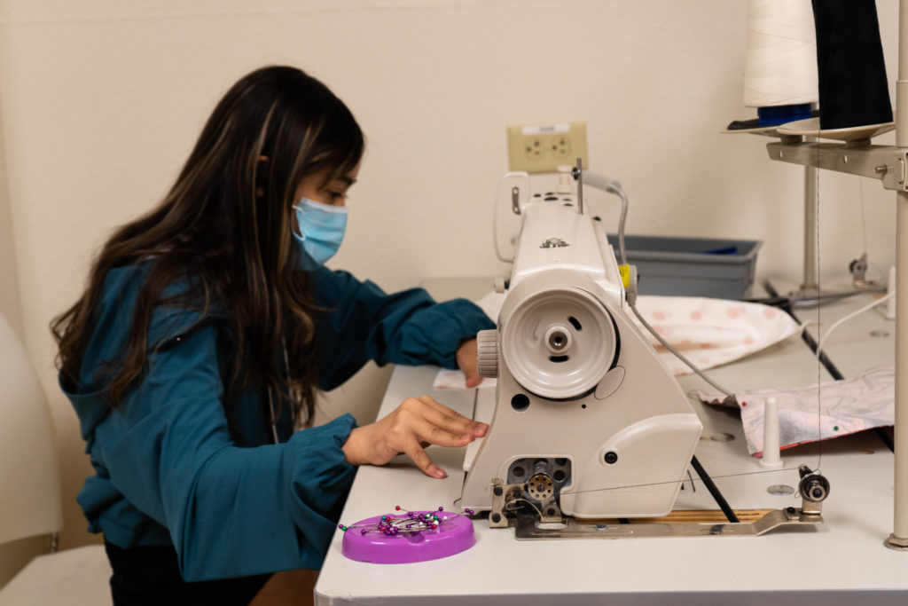 A student sits at a sewing machine constructing a garment.