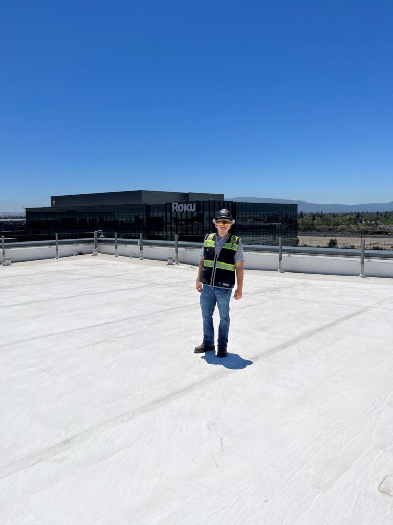 Adrian Contreras stands on the roof of the Roku construction site wearing construction gear.