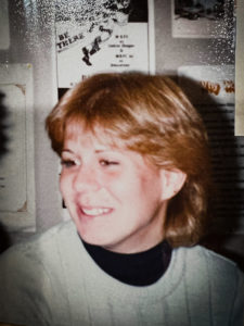 A snapshot of a young woman in the 1980s with event posters behind her