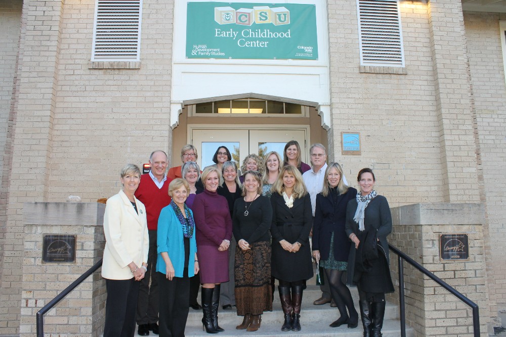 A group of 16 adults stand on the steps of a school building, with a green banner above that says CSU Early Childhood Center.