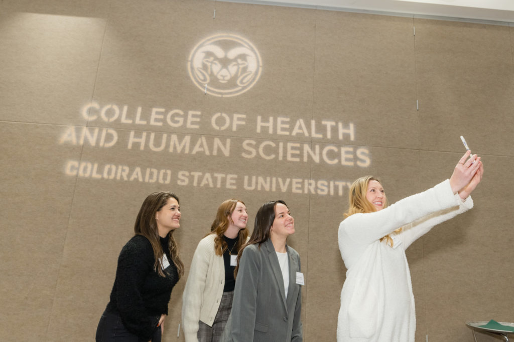 Four people posing for a selfie in front of College of Health and Human Sciences sign