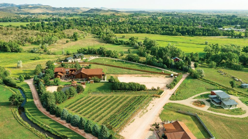 Aerial view of a lush, green vineyard with a winery and event venue, and Colorado foothills in the background.