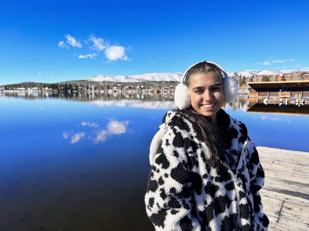 Rebeca Naredo standing on a pier in front of a calm lake with mountains in the background