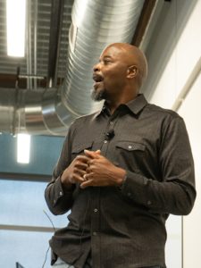 A Black man in a black shirt speaking in a classroom