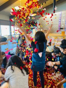 A group of children surround a pile of flower petals. One child throws them in the air.