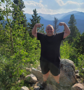 Wesley Brookshear with his arms rasied above his head and mountains behind him in the distance