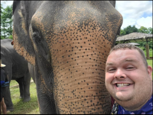 Wesley Brookshear standing next to an elephant's trunk in Thailand.