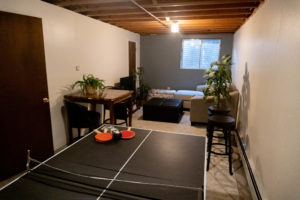 A common room with couches, a tv, a table with stools, and a ping pong table.