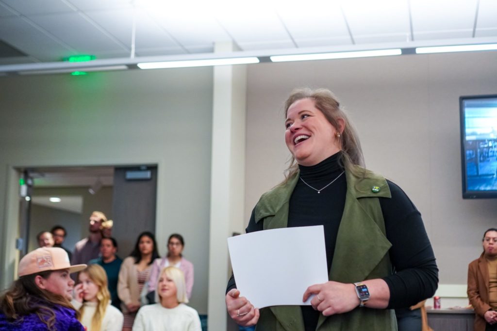 Professor Kristen Morris smiles in admiration as she talks about her students and their accomplishments in the center of a room filled with program attendees