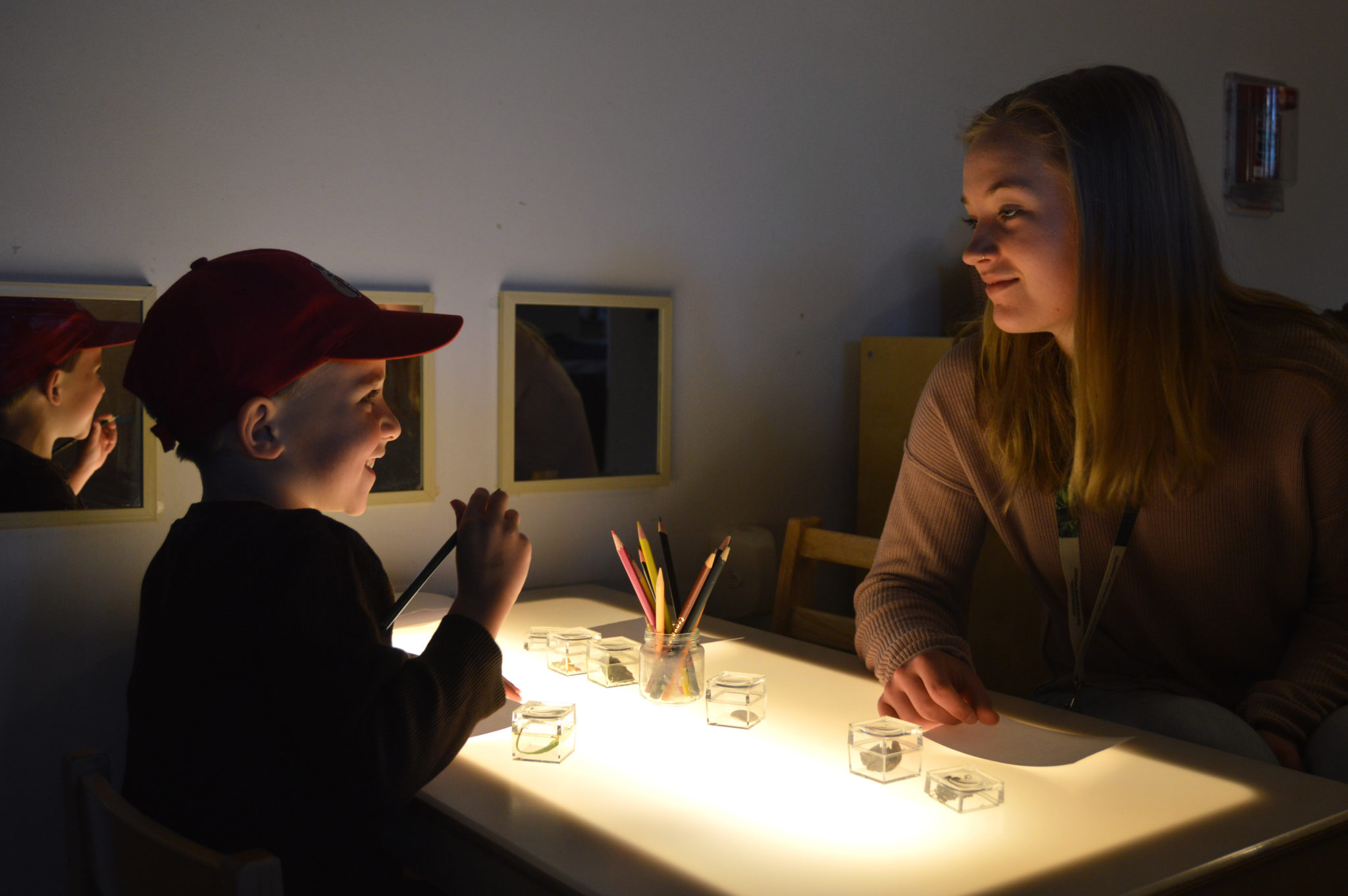 a student teacher and young child smile as they do an activity at an illuminated table in a dark room.