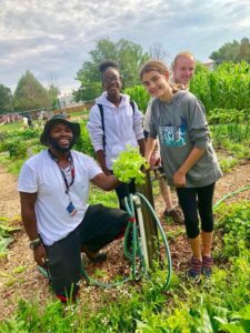 Robert Wiggins in a garden with students. They are holding lettuce from the garden and standing at a water spigot.
